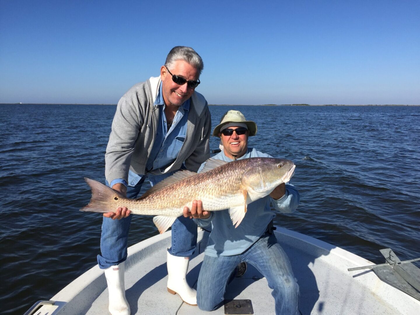 Two men holding a large fish on the water.