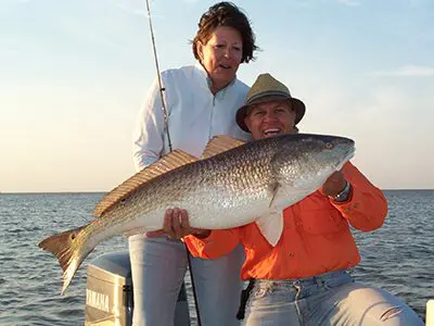 A couple of people holding up a fish on top of a boat.