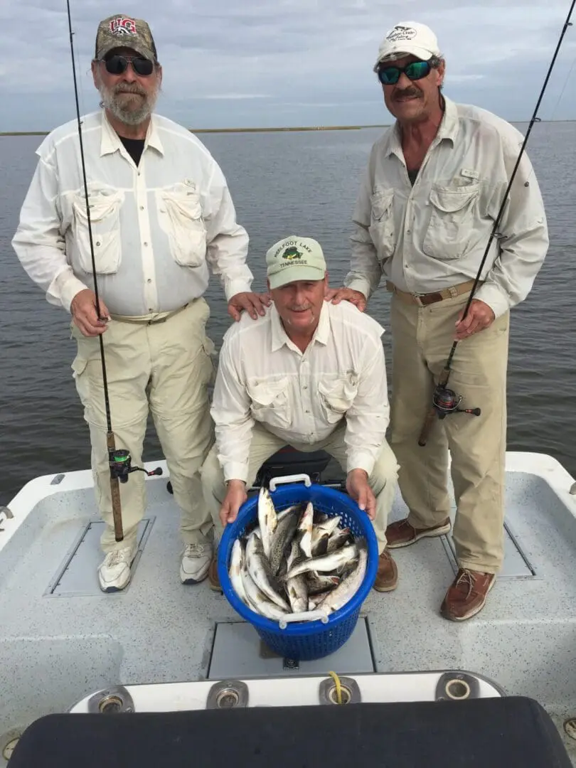 Three men are holding a blue bucket with fish in it.