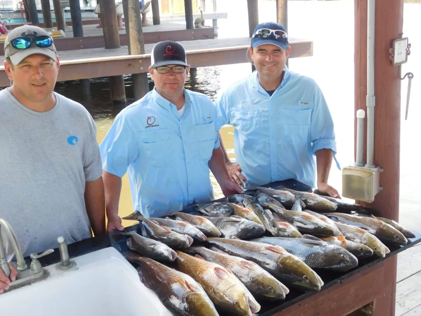 Three men standing next to a table of fish.