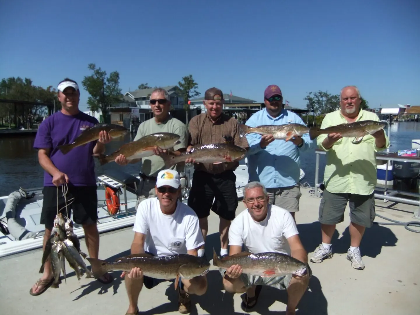 A group of men holding up fish on top of a dock.